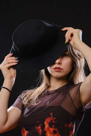 young serious woman in black hat looking at camera on black backgroundの写真素材