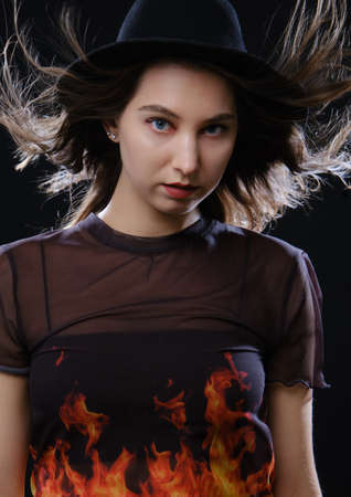 young serious woman in black hat looking at camera on black background