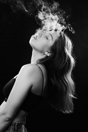 woman with closed eyes blowing smoke on black background, monochromeの写真素材