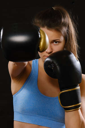 Pretty Muay Thai female boxer in attack pose. Fitness young woman boxing training on black background, closeupの写真素材
