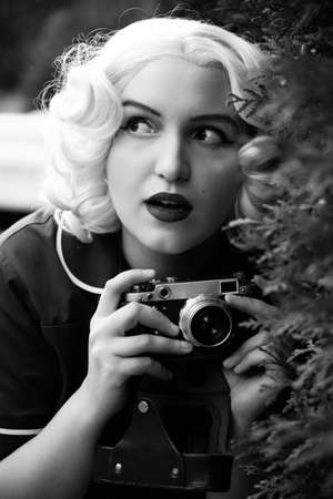 young blond woman with old-style photo camera looking aside, monochrome