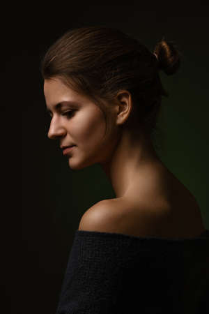 beautiful female portrait with bare shoulders side profile view on dark backgroundの写真素材