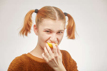 fun girl eats lemon on white background, grimacingの写真素材