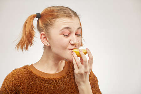 fun girl eats lemon on white background, grimacingの写真素材