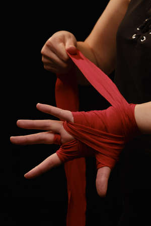 Muay Thai female boxer wearing strap on wrist closeup view. Fitness young woman preparing for boxing training on black backgroundの写真素材
