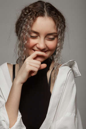 shy young woman with curly hair looking at camera, white background