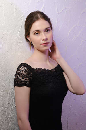 Young beautiful brunette young woman in a black evening dress on the background of white wall...