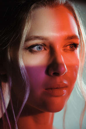 serious beautiful young woman with bare shoulders looking aside on multicolor background, closeup...