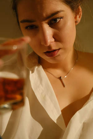 Young woman drinking alcohol from glass against sunny wall background, addictionの写真素材