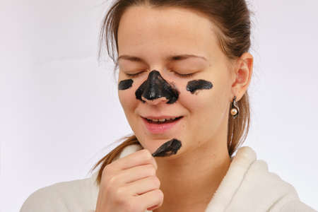 Fun young woman removing blackheads on her face with cosmetic patches on white background
