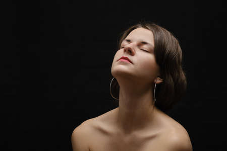 Black and white shot of woman with bare shoulders posing sensually holding head up on black backgroundの写真素材
