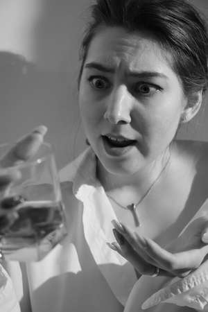 Young woman drinking alcohol from glass against sunny wall background, addiction. monochrome imageの写真素材