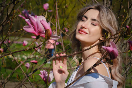 Happy woman smiling at magnolia tree with blossoming flowersの写真素材