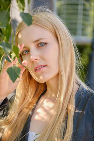 cute blond girl with green eyes closeup portrait in birch leaves