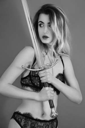 woman in black lingerie posing with sword on gray background in studioの写真素材