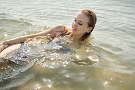 young blond woman in swimsuit at sea surf with foam relax