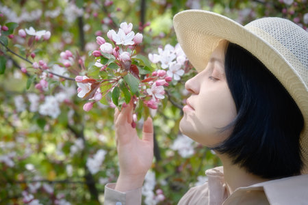 beautiful young woman in sunhat near cherry blossoms close up portraitの写真素材