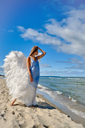 A young beautiful woman angel with white wings on sea beachの写真素材