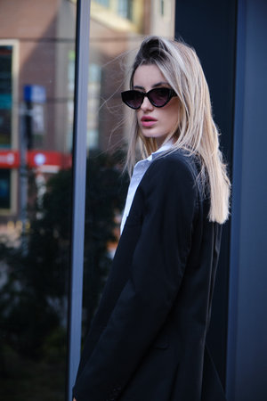 A young stylish blonde woman in a trendy outfit is walking on a European street. street fashionの写真素材