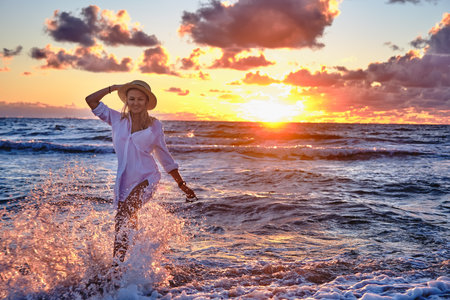 carefree woman in straw hat posing in the sunset on the sea beach. Vitality healthy living concept. Girl in pareo on sunset at stormy sea.の写真素材