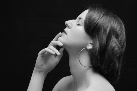 Black and white shot of woman with bare shoulders posing sensually holding head up on black background monochromeの写真素材