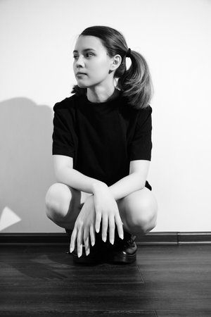 sad girl in black bodysuit and male boots sitting on floor monochromeの写真素材