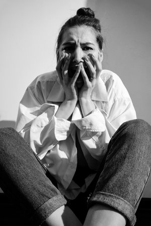 serious young woman feeling sad and scared, depressed. Sitting on white background with shadow monochromeの写真素材