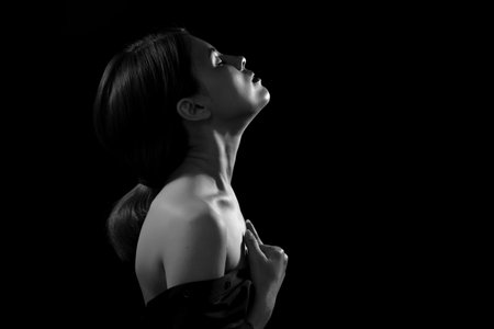 sensual serious woman with bare shoulders, closed eyes in multicolor lights on black background...