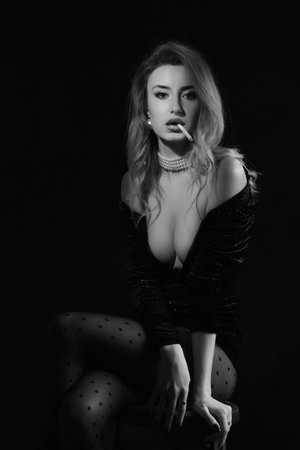 luxury woman in black dress with cleavage smoking cigarette on black background monochromeの写真素材
