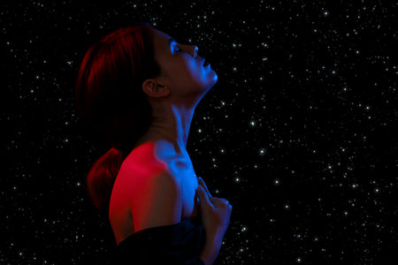 sensual serious woman with bare shoulders, closed eyes in multicolor lights on stars background