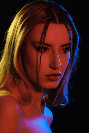 sensual young blond woman with bare shoulders on black background in multicolored light