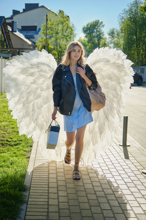 A young beautiful woman angel with white wings walks on the street