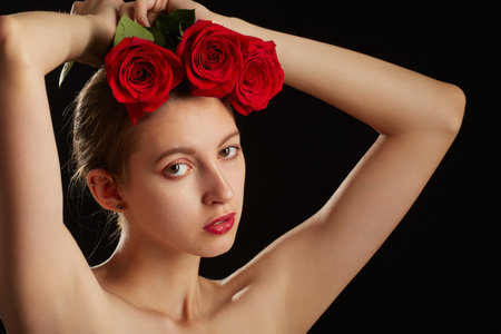 beautiful young woman with red rose, natural beautiful makeup looking at camera on a black backgroundの写真素材