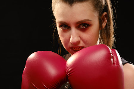 Pretty Muay Thai female boxer with bruise on face in attack pose. Fitness young woman boxing training on black backgroundの写真素材