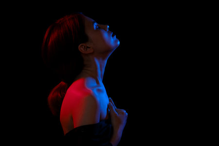 sensual serious woman with bare shoulders, closed eyes in multicolor lights on black backgroundの写真素材