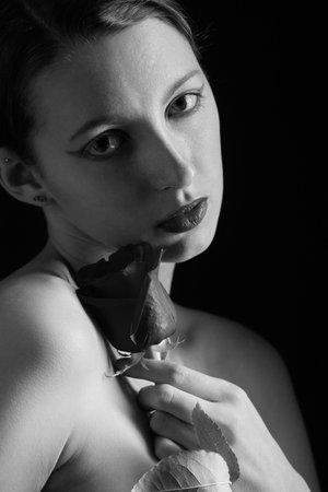 beautiful young woman with black rose, natural beautiful makeup looking at camera on a black background monochromeの写真素材