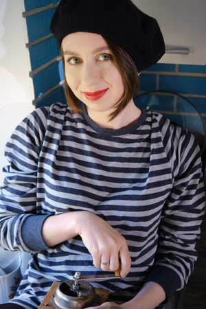 happy young woman grinds coffee with a handmade old mill in the kitchen, looking at cameraの写真素材