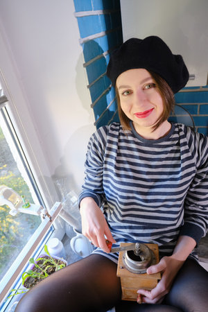 happy young woman grinds coffee with a handmade old mill in the kitchen, looking at camera