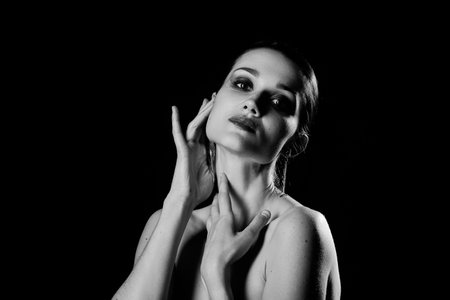Black and white shot of young woman posing sensually holding head up on black background, closed eyes, monochromeの写真素材