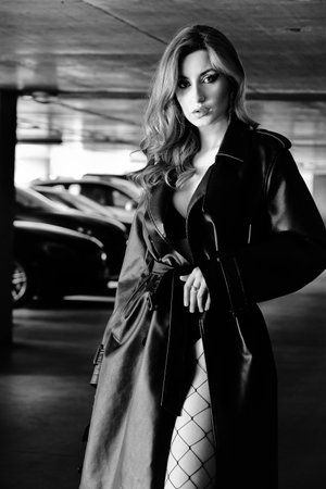young woman in leather coat at parking garage posing with cars on background monochromeの写真素材
