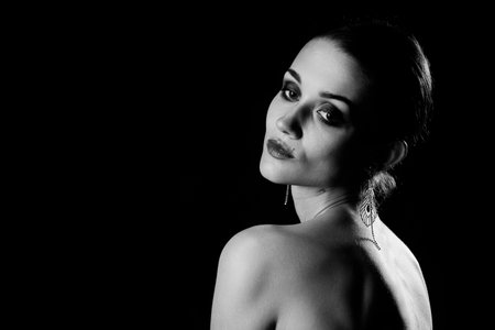 beautiful sad female silhouette with bare shoulders on black background with copy space, rear view monochromeの写真素材