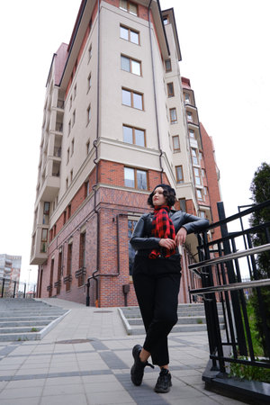 European pretty young hipster woman in a trendy leather coat in black trousers is standing near a vintage building in the city. Beautiful stylish girl on a walk. Stylish women's clothing.の写真素材