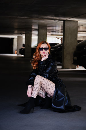 young woman in leather coat at parking garage posing with cars on background
