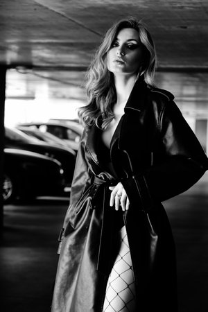 young woman in leather coat at parking garage posing with cars on background monochromeの写真素材