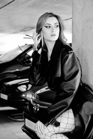 young woman in leather coat at parking garage posing with cars on background monochromeの写真素材