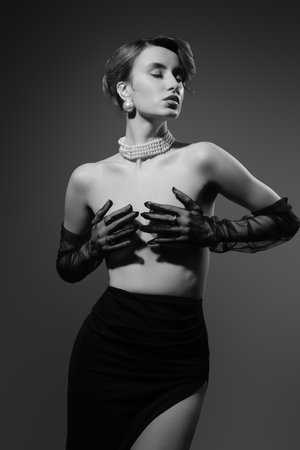 Beautiful luxury young woman with clean skin covering her bare breast. Studio gray background monochromeの写真素材