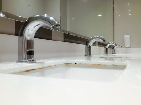 Empty public toilet room with sinks and taps.