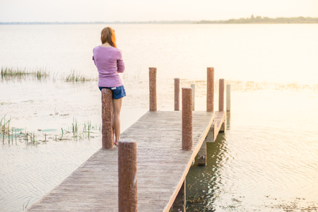 young girl is sitting on a wooden bridgeの写真素材