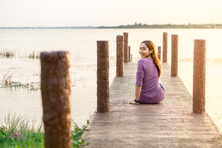 young girl is sitting on a wooden bridgeの写真素材