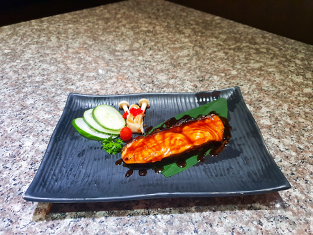 Grilled salmon with vegetables served on black stone plate on wooden tableの写真素材